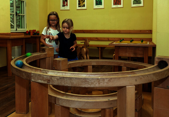 Das Bild zeigt zwei Mädchen, die mit einer Kugelbahn im Spielzimmer des Hunsrücker Holzmuseums spielen.