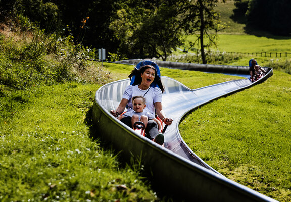 Das Bild zeigt eine Frau und einen Jungen, die die Sommerrodelbahn beim Freizeitzentrum Peterberg fahren.