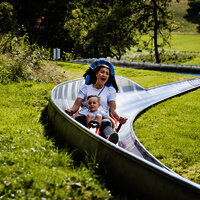 Das Bild zeigt eine Frau und einen Jungen, die die Sommerrodelbahn beim Freizeitzentrum Peterberg fahren.