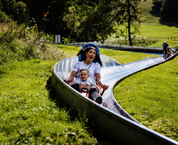 Das Bild zeigt eine Frau und einen Jungen, die die Sommerrodelbahn beim Freizeitzentrum Peterberg fahren.