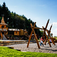 Das Bild zeigt Kinder, die auf de Spielplatz mit Rutschen, Schaukeln und Klettergerüsten spielen.