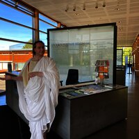 Das Bild zeigt eine römische Figur und die Dauerausstellung im Kulturzentrum Belginum Archäologiepark.