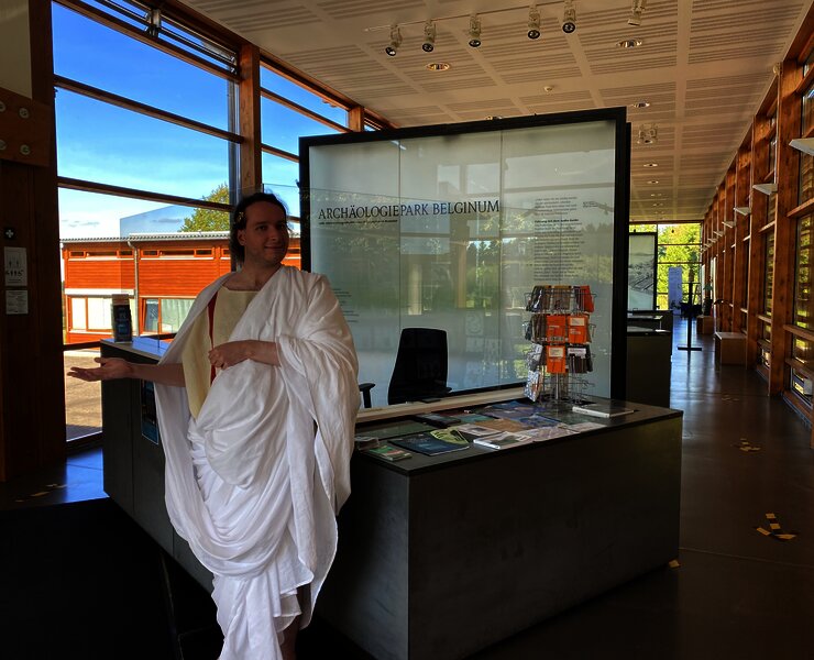 Das Bild zeigt eine römische Figur und die Dauerausstellung im Kulturzentrum Belginum Archäologiepark.