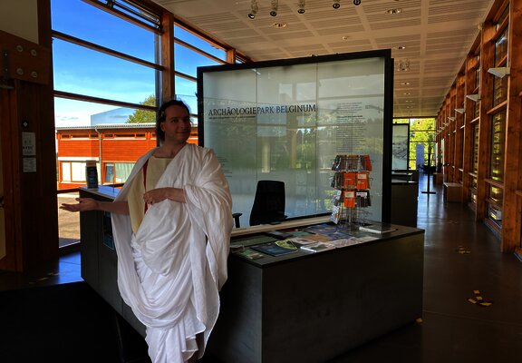 Das Bild zeigt eine römische Figur und die Dauerausstellung im Kulturzentrum Belginum Archäologiepark.