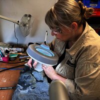 Das Bild zeigt eine Paläontologin, die mithilfe einer Lupe und Werkzeugen an Fossilien arbeitet.