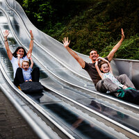 Das Bild zeigt zwei Erwachsene und zwei Kinder, die auf einer Teppichrutsche beim Freizeitzentrum Peterberg rutschen.