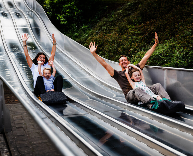 Das Bild zeigt zwei Erwachsene und zwei Kinder, die auf einer Teppichrutsche beim Freizeitzentrum Peterberg rutschen.