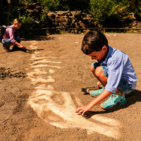 Das Bild zeigt zwei Kinder im Dinopark Teufelsschlucht, die auf einer Sandfläche ein Dinoskelett ausgraben.