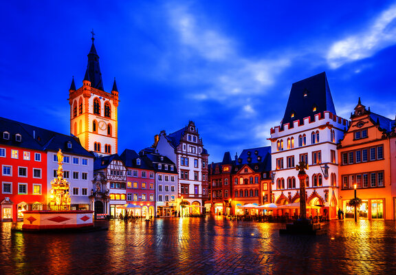 Das Bild zeigt einen alten Platz mit schön verzierten Häusern in Trier bei Abendstimmung- und beleuchtung.