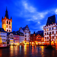 Das Bild zeigt einen alten Platz mit schön verzierten Häusern in Trier bei Abendstimmung- und beleuchtung.
