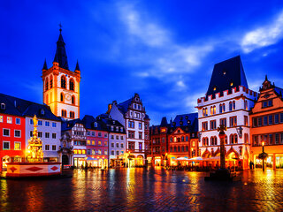 Das Bild zeigt einen alten Platz mit schön verzierten Häusern in Trier bei Abendstimmung- und beleuchtung.