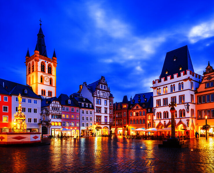 Das Bild zeigt einen alten Platz mit schön verzierten Häusern in Trier bei Abendstimmung- und beleuchtung.