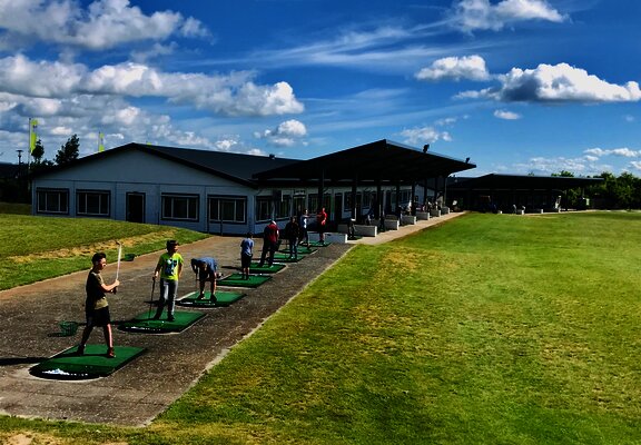 Blick auf die Abschlag Anlage des Golfclub Cochem, auf dem Personen Bälle schwingen.